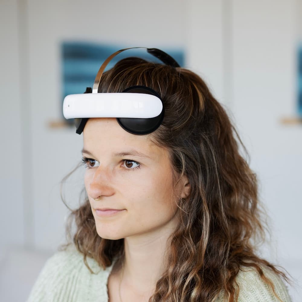 Frau mit lockigem Haar trägt ein modernes Flow Neuroscience Headset auf der Stirn, in einem hellen Raum mit entspannter Atmosphäre.